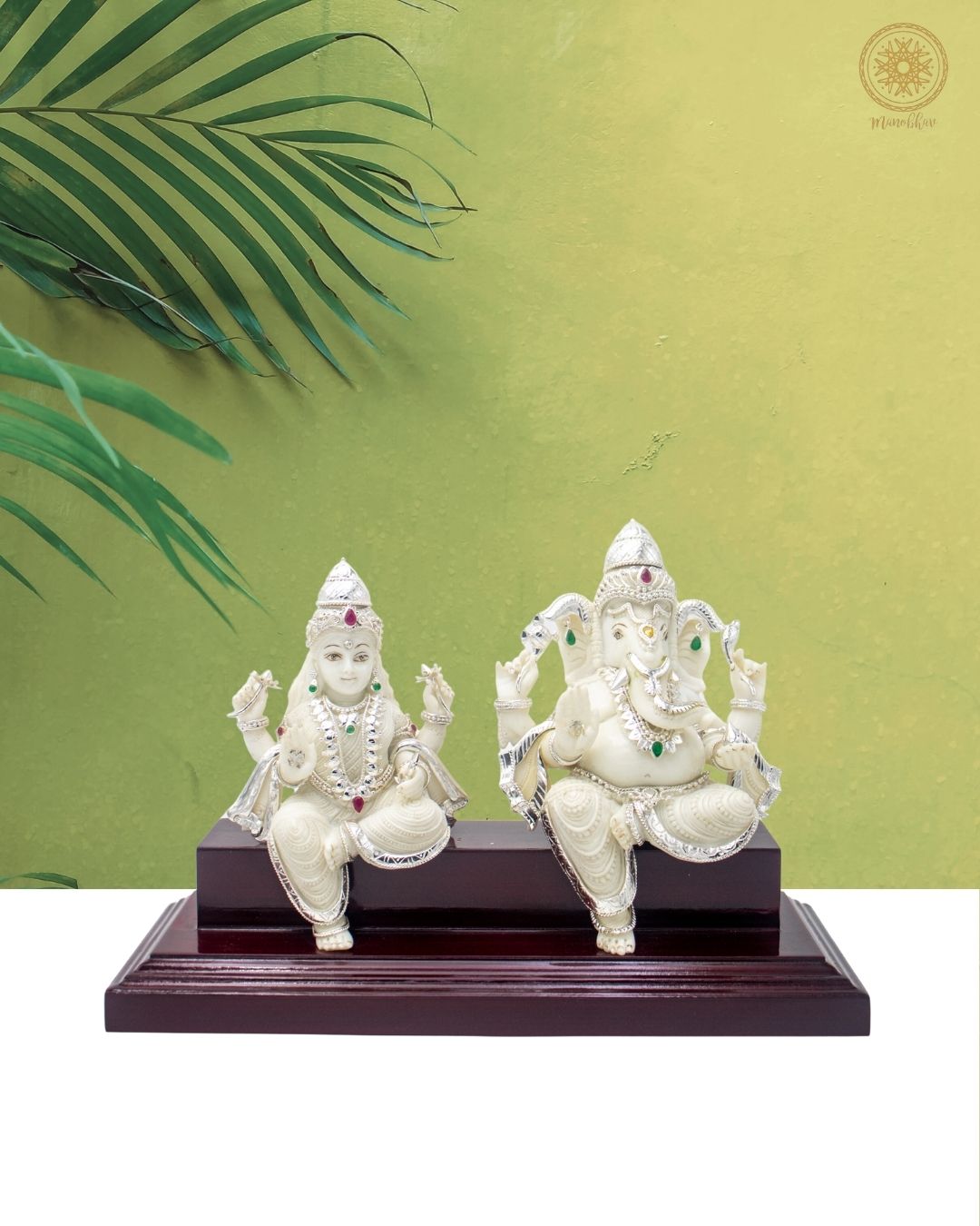 White Ganesh and Laxmi statues with jewelry on a wooden base against a green background